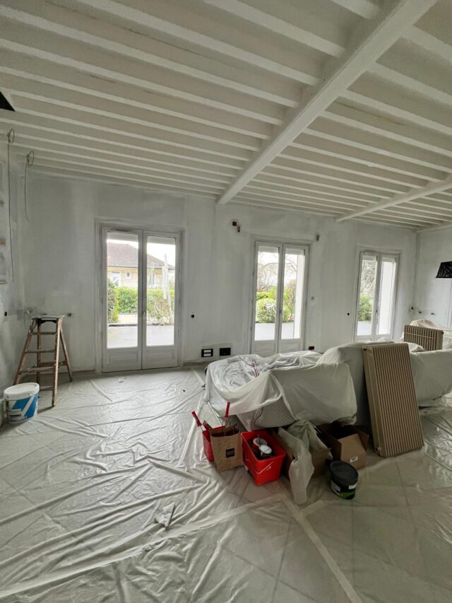Photo d'une grande pièce protégée par des plastiques dans le cadre d'un chantier de peinture.