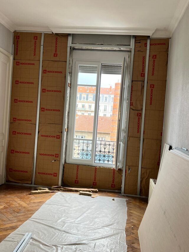 Photo d'un mur intérieur en train d'être isolé avec de laine de verre posée sur rail de placo.