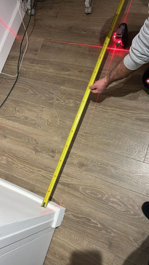 Photo d'une opération de mesure avec un mètre ruban et un pointeur laser.
