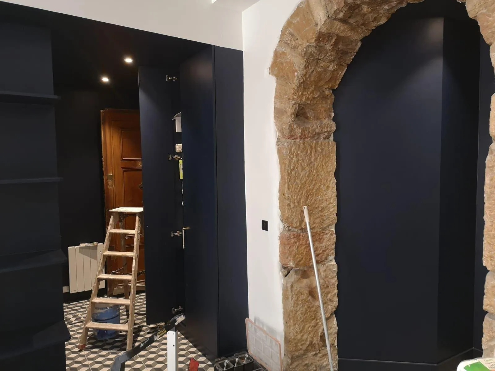 Photo d'un intérieur moderne avec un arche de porte en pierre, des murs blancs et des placards de couleur noire.