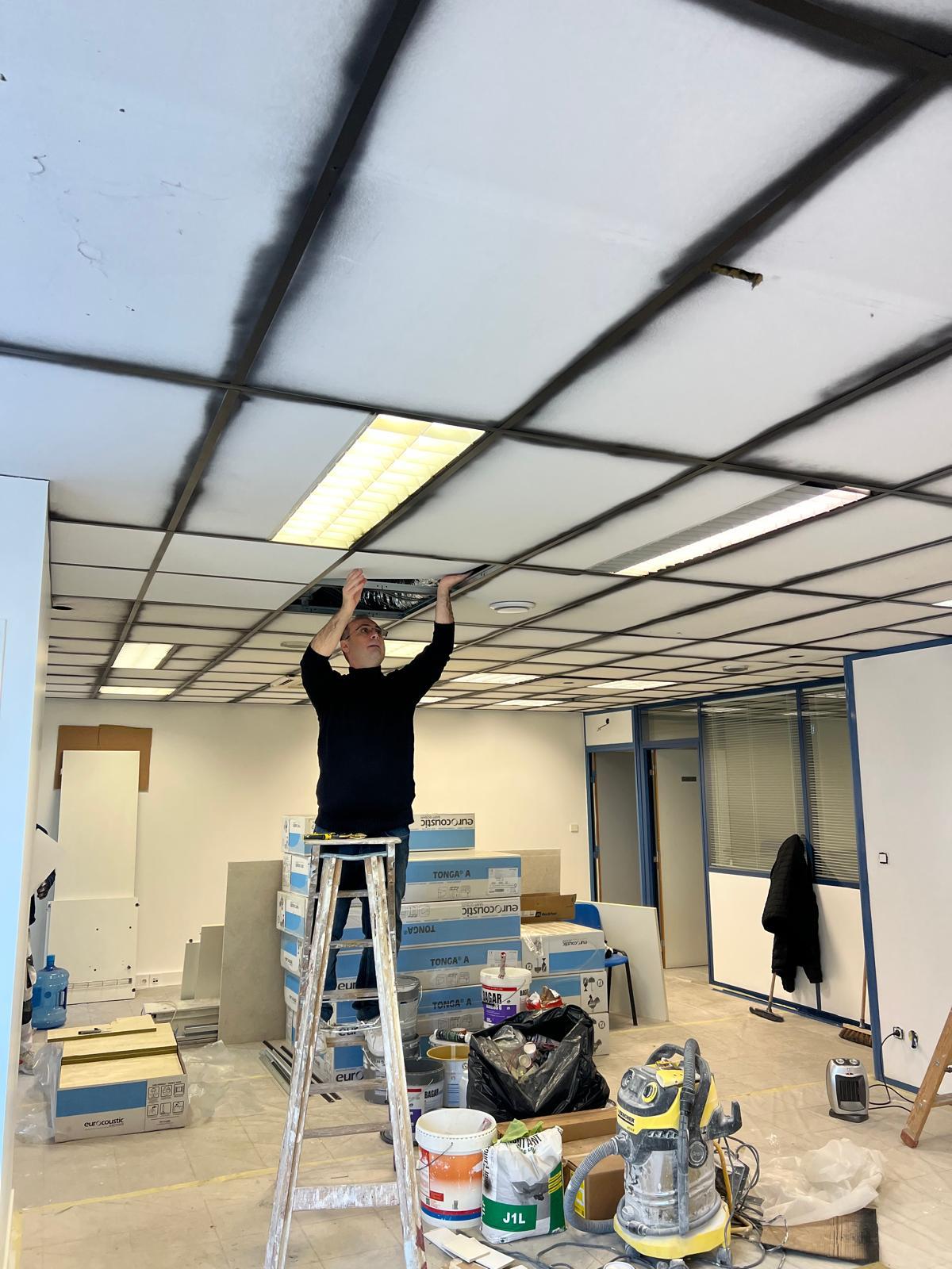 Photo d'un ouvrier du bâtiment en train de fixer des dalles d'un plafond suspendu.