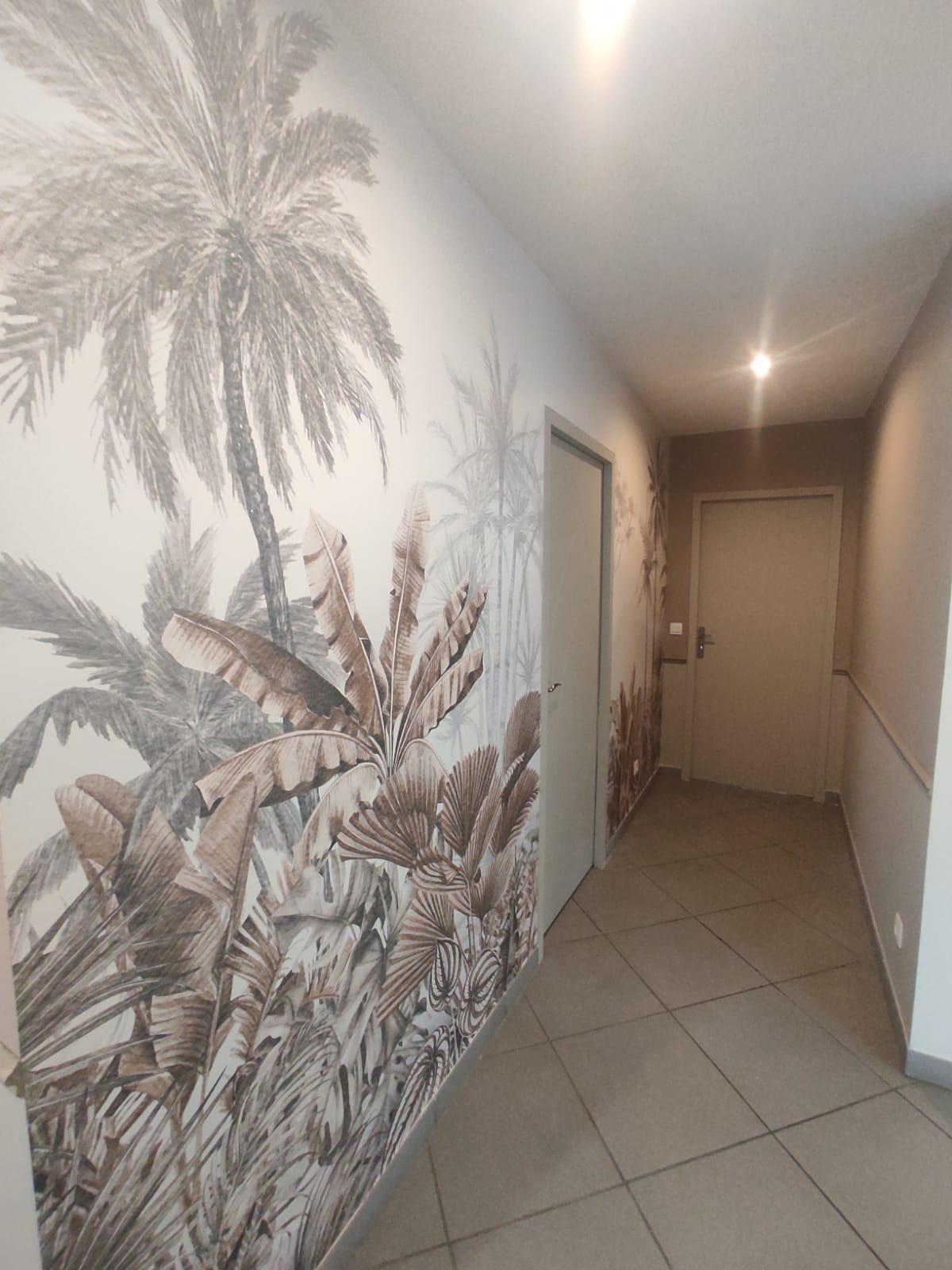Photo d'un couloir dont l'un des murs est recouvert d'un papier peint grande dimension représentant des palmiers.