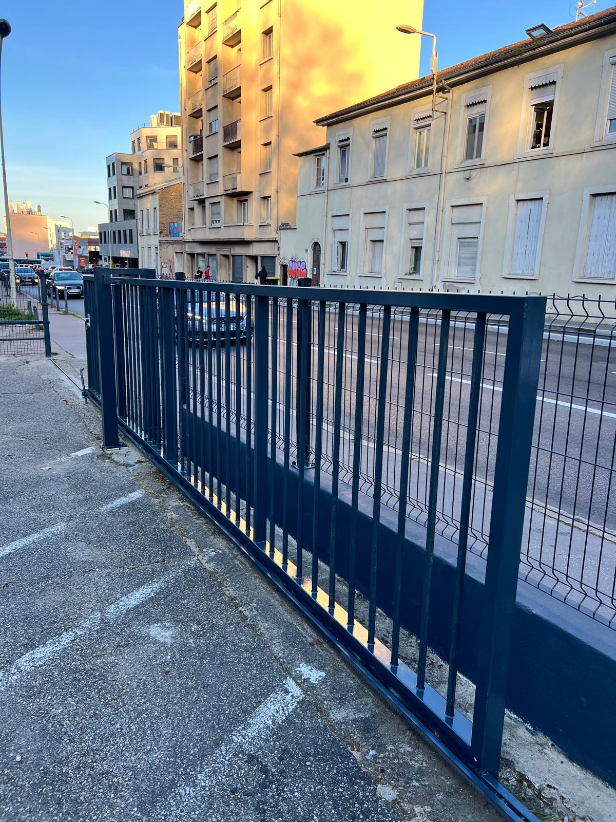 Photo d'un portail coulissant de couleur noire situé à l'entrée d'un immeuble situé en pleine ville.