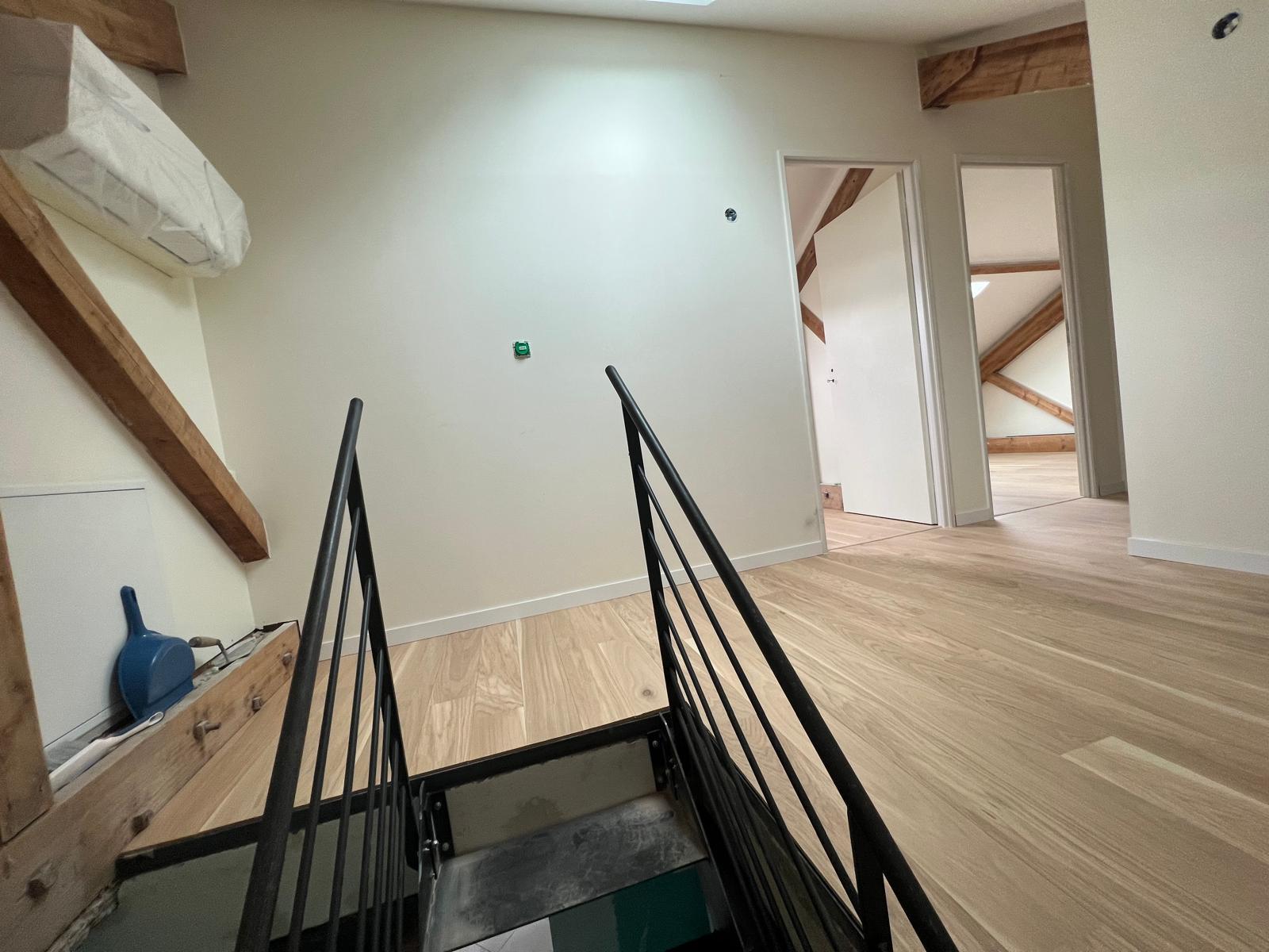 Photo d'un escalier industriel donnant sur des combles aménagés de manière moderne avec du bois et des teintes claires.