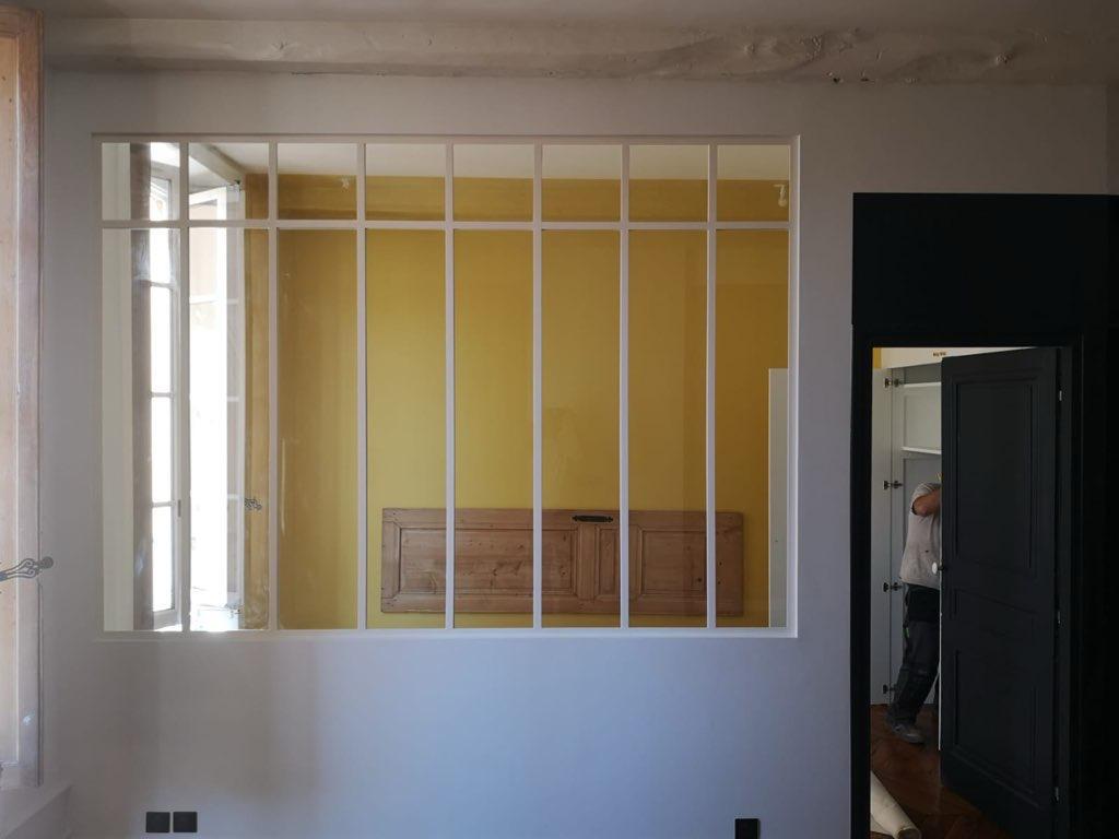 Photo d'une verrière industrielle de couleur blanche dévoilant un mur de couleur jaune en arrière plan.