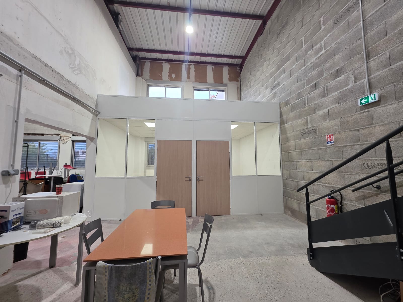 Photo de l'intérieur d'un entrepôt avec une table, des chaises, un micro-onde et une pièce fermée par des doubles portes.