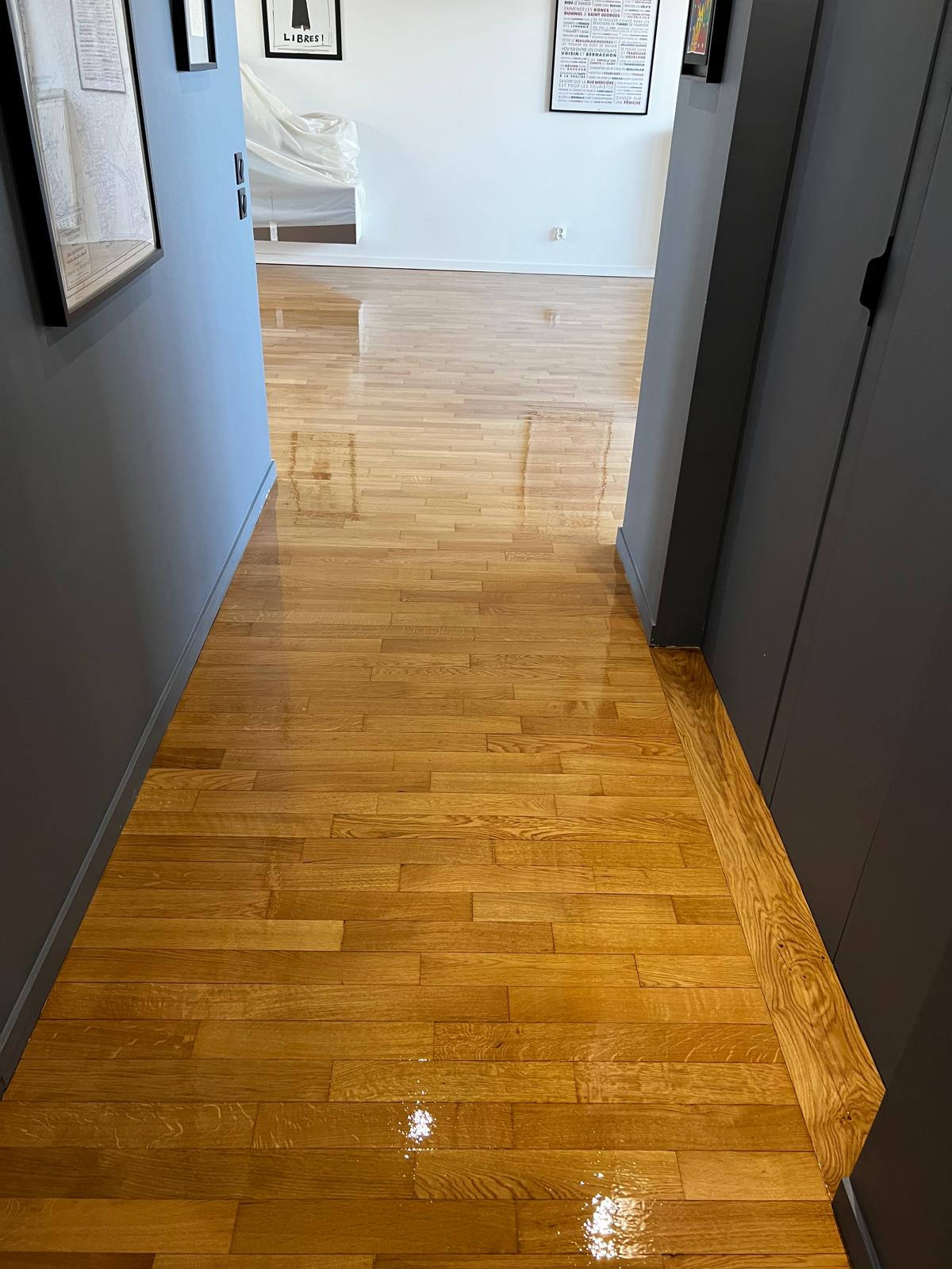 Photo d'un couloir où des murs sombres mettent en valeur un parquet à la française qui a été récemment vernis.