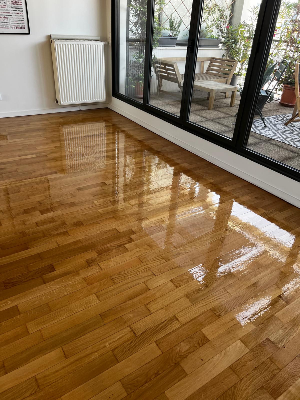 Photo d'un parquet lustré à lattes fines de merisier devant une véranda aux cadres noirs.