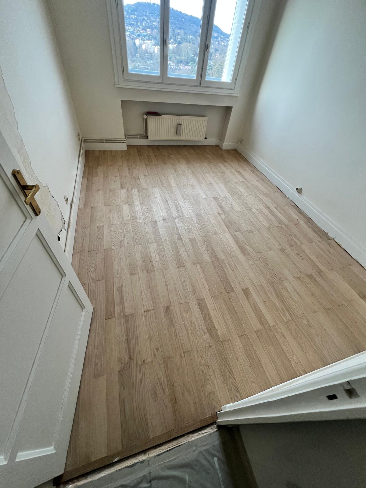 Photo d'une chambre d'appartement aux murs blancs avec un parquet en lattes de chêne clair.