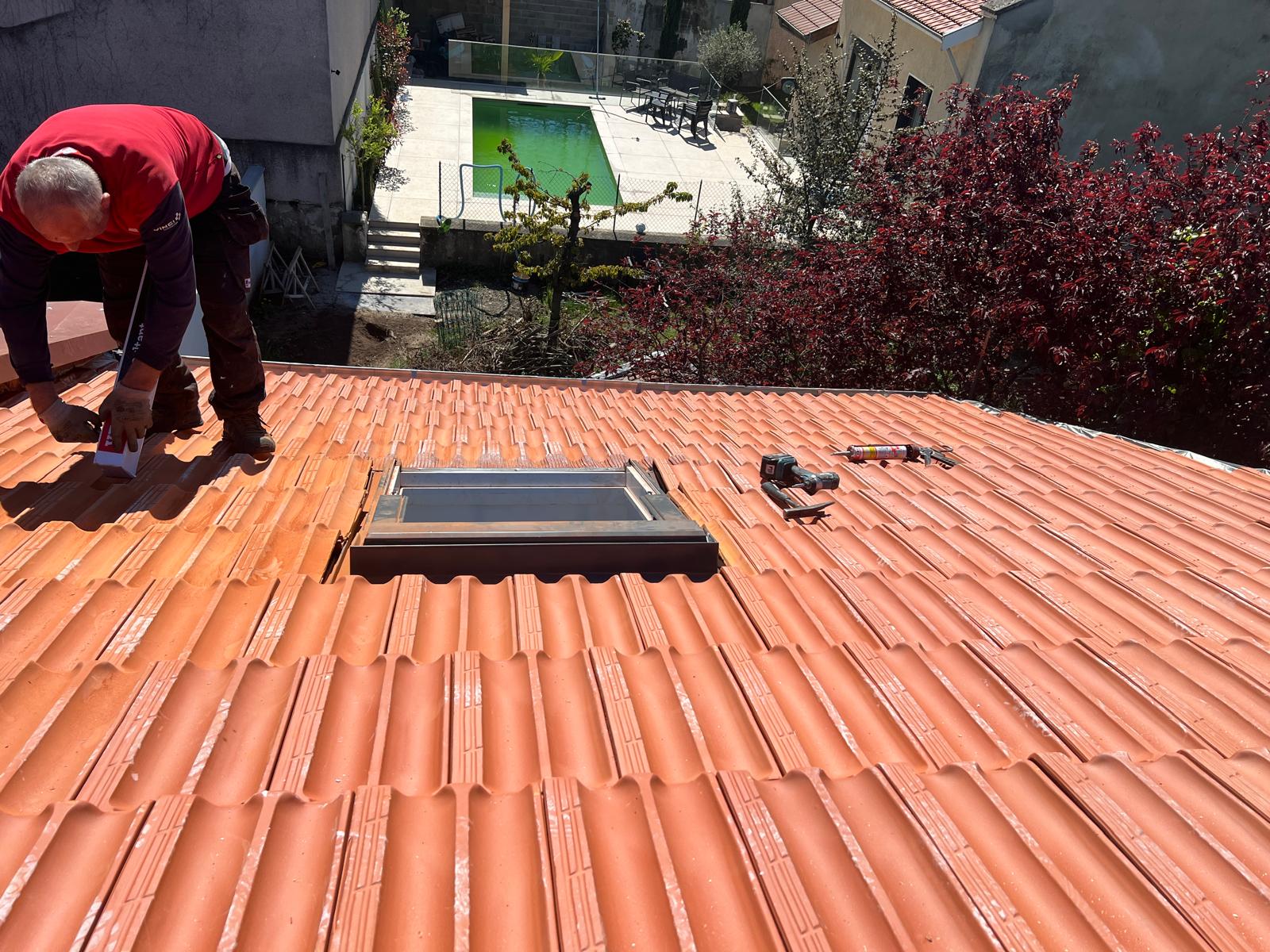 Photo d'un couvreur intervenant sur un toit de tuiles plates rouges.